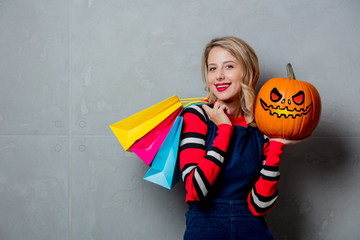 Young style girl in jeans clothes with shopping bags and halloween pumpkin on grey background.