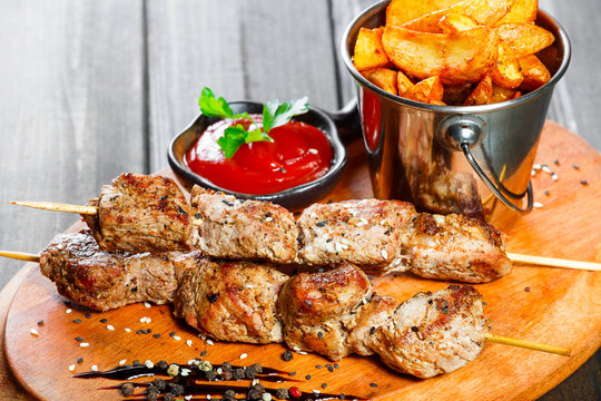 Skewers of Meat with sauce and potatoes fries in a bucket on wooden cutting board