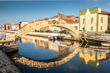 Fototapeta na wymiar Carcavelos bridge on the São Roque canal, in the city of Aveiro, Portugal, with houses in the background and reflection in the water.