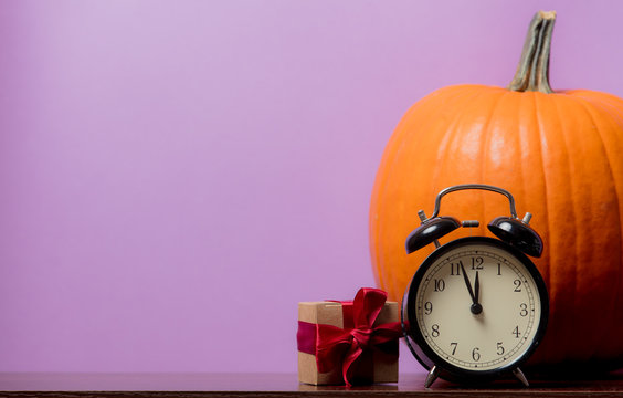 one orange pumpking and vintage alarm clock with gift box on purple background