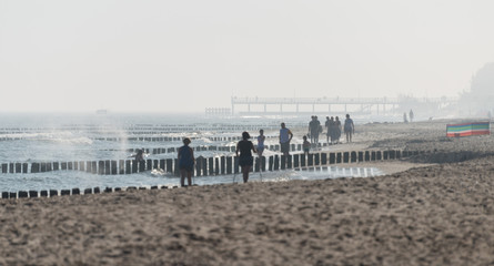 Fototapeta na wymiar Kolobrzeg, Poland 28 Juli 2018. Misty morning on the Polish beach visible people, sea, screens and wooden breakwaters.