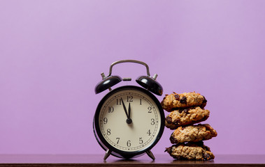 Christmas oat cookie and vintage alarm clock on purple background