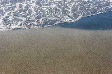 sea waves on black sand near water on the beach. Background texture.