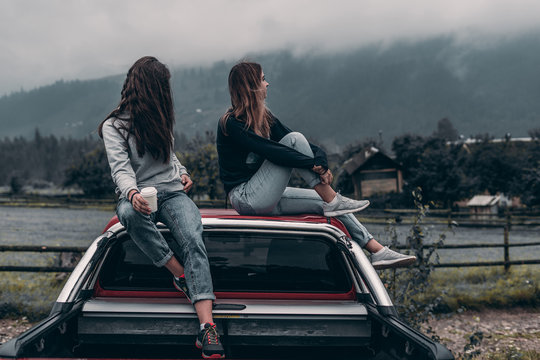 two girls are sitting by the car on a mountains background.