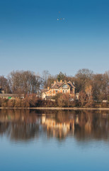 Old house over water. Reflection of a house in the river. Landscape with the house and trees displayed in the water_