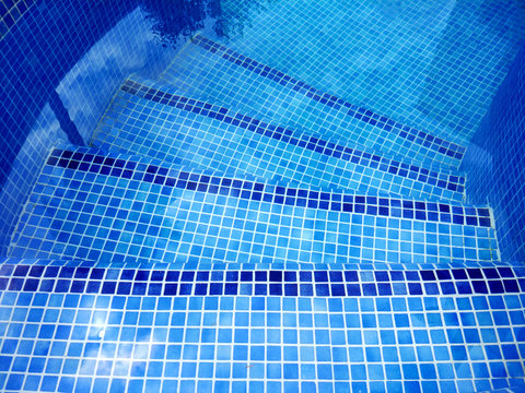 Top view of swimming pool curved stairs in two tones of blue color with tree reflection on the water