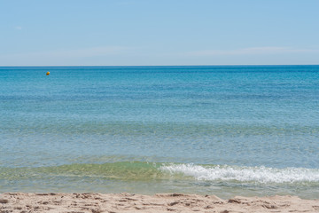 Clear blue water at a sandy beach in the Mediterranean Sea in Spain. Small wave at the sea on a summer day with clear sky