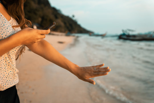 happy young woman on beach photographing her engagement ring after wedding proposal