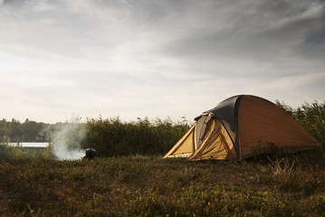 Tent on the shore of the lake near a burning fire with a kettle.