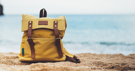 Hipster hiker tourist yellow backpack closeup on background blue sea ocean horizon on sand beach,...