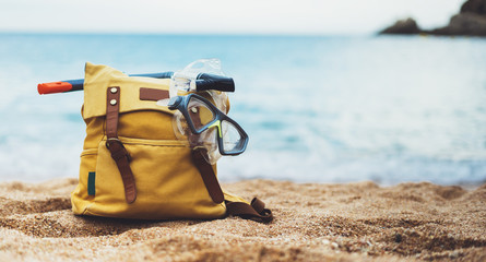 Hipster hiker tourist backpack and swimming mask on background sea ocean horizon on sand beach, blurred panoramic seascape blank, traveler relax holiday concept, sunlight view in trip vacation