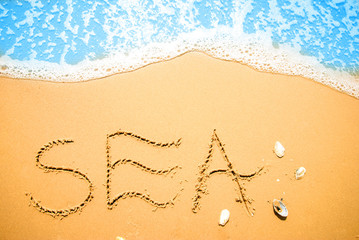 Word SEA written on the beach sand, with a blue wave