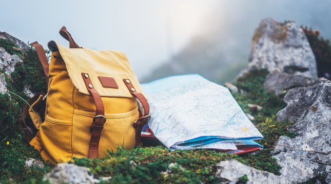 Hipster hiker tourist yellow backpack and map europe on background green grass nature in mountain, blurred panoramic landscape, traveler relax holiday concept, view planning wayroad in trip vacation
