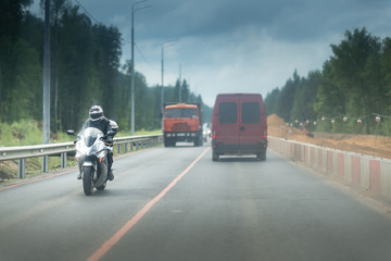 city traffic with a motorbike and cars. Road with white and red concrete barriers or block. Part of the highway is under construction. Left side have a metal safety barrier or rail