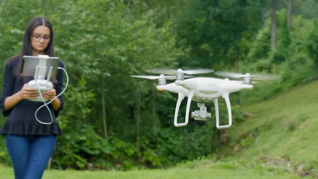 Young woman controlling drone in field. Drone operator holding a transmitter remote control and digital tablet computer outdoors. 4k