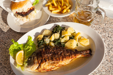 Grilled fish and potatoes with spinach with fries and burger in the background