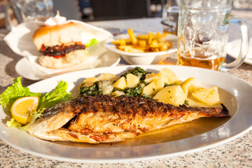 Grilled fish and potatoes with spinach with fries and burger in the background