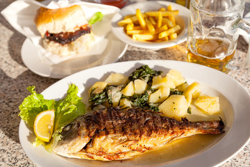 Grilled fish and potatoes with spinach with fries and burger in the background