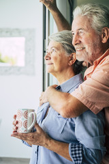 beautiful aged caucasian couple man and woman looking outside the window at home ina romantic...