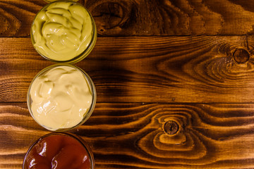 Different sauces in glass bowls on wooden table. Top view