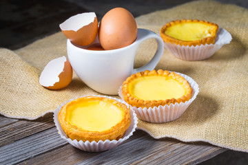 Egg tarts and eggs on burlap and wooden surface 