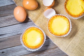 Egg tarts and eggs on burlap and wooden surface 