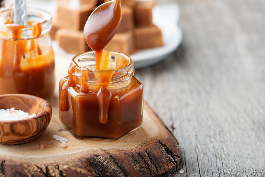 Homemade salted caramel sauce in jar on rustic wooden table.