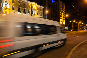 Motion blurred white minibus on the street in the evening. - obrazy, fototapety, plakaty
