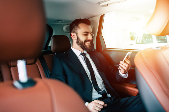 Good news! Handsome smiling business man with mobile phone on hand in car