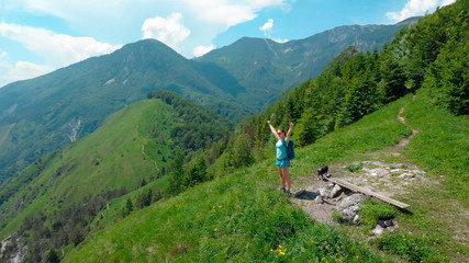 Fototapeta na wymiar AERIAL: Joyful female hiker celebrates a successful ascent of mountain in Alps.