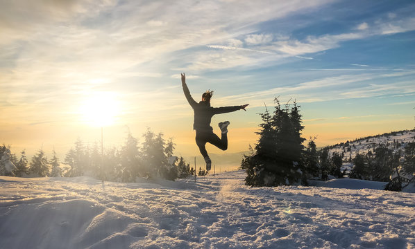 Silhouette of a jumping woman on a snowy hill in sunset