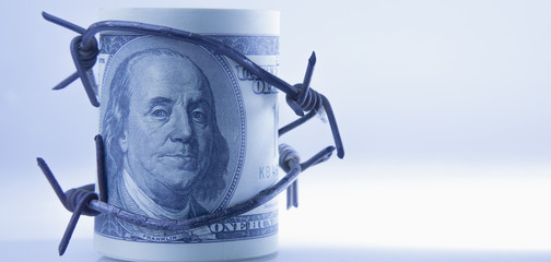 US Dollar money wrapped in barbed wire as symbol of economic warfare, sanctions and embargo busting