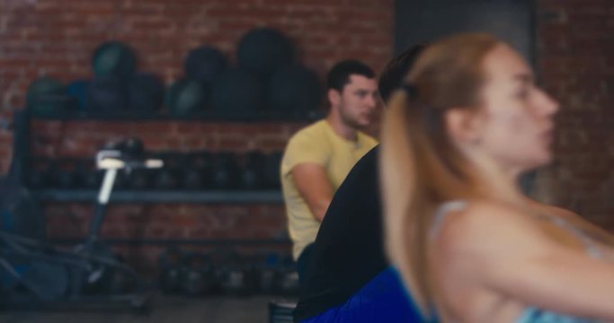 Three athletes working out in a gym, using rowing ergometers indoors. 4K UHD