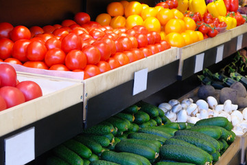 Various vegetables tomatoes, cucumbers, peppers, mushrooms are sold at vegetable shop. Vegetables lie on shelf in grocery store.
