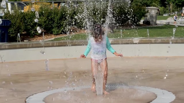 Girl runs through a splash pad water fountain in slow motion.