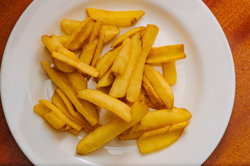 French potatoes fries in the white plate on wooden background.