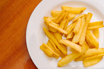 French potatoes fries in the white plate on wooden background.