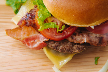 Close-up photo of home made delicious burger stacked high with a juicy beef patty, cheese, fresh lettuce, onion and tomato on a fresh bun with sesame seed standing on wooden table.