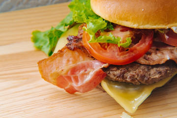 Close-up photo of home made delicious burger stacked high with a juicy beef patty, cheese, fresh lettuce, onion and tomato on a fresh bun with sesame seed standing on wooden table.