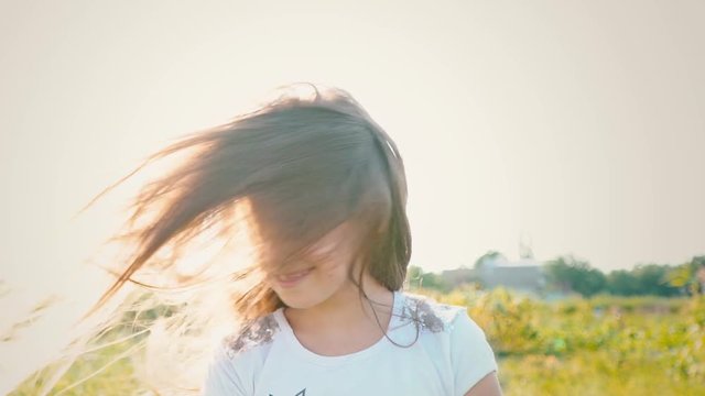 An attractive little girl with long flowing hair twists her head in different directions, the wind develops long hair of the child