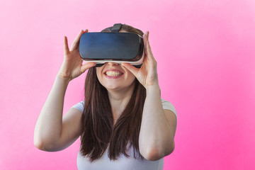 Smile happy young woman wearing using virtual reality VR glasses helmet headset on pink background. Smartphone using with virtual reality goggles. Technology, simulation, hi-tech, videogame concept