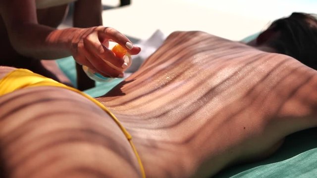 Spraying sunscreen on topless sunbather, slow motion close up