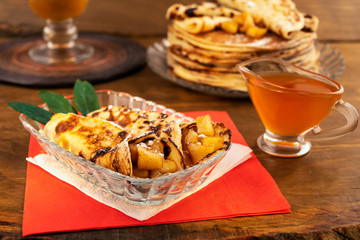 Fried pancakes with apple  filling, honey in a glass gravy boat, a stack of pancakes in the background, all on a wooden background.