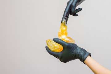 sugar paste or wax honey for hair removing with black gloves hands of cosmetologist in spa salon -...