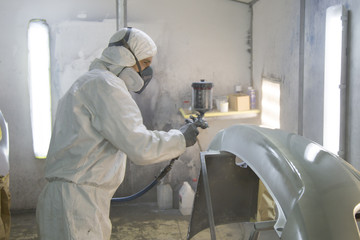 auto mechanic worker painting car in a paint chamber during repair work