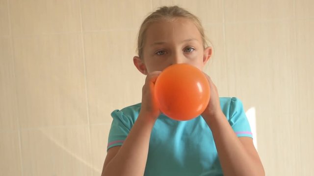 Happy girl in blue t-shirt inflates a bright orange ball in bathroom at home. Shallow focus