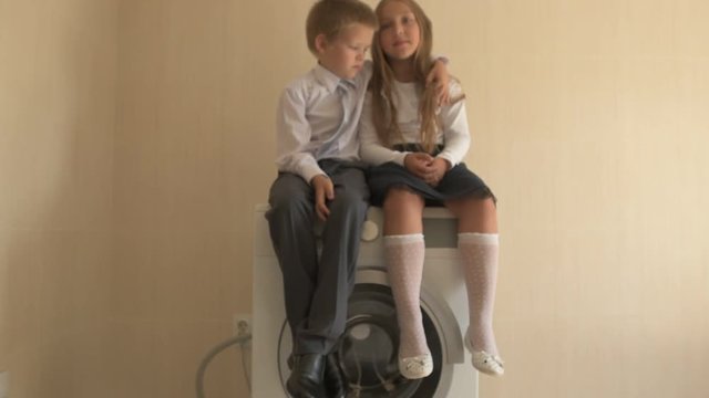 Back to school. Portrait of happy children with blue eyes and blond hair in school uniform. Boy and a preschool girl sitting on washing machine at home in bathroom. Shallow focus