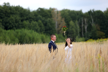 Młoda para na łące łapie bukiet ślubny z czerwonych róż.