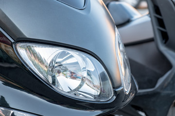A headlight of a black scooter.