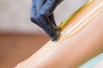 procedure of hair removing on leg beautiful woman with sugar paste or wax honey and black gloves hand - depilation and beauty concept - obrazy, fototapety, plakaty